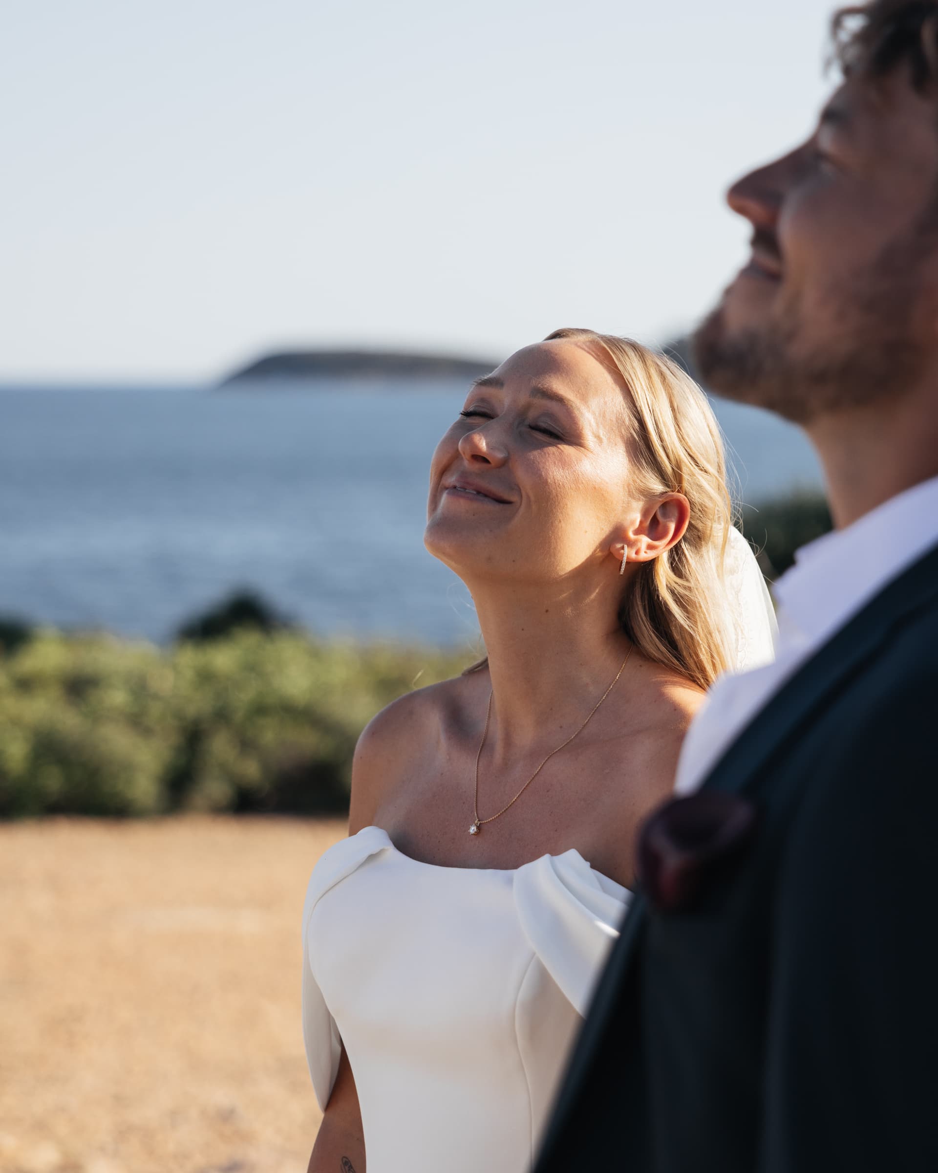 Profile portrait of a person in a white wedding dress with the sea behind.
